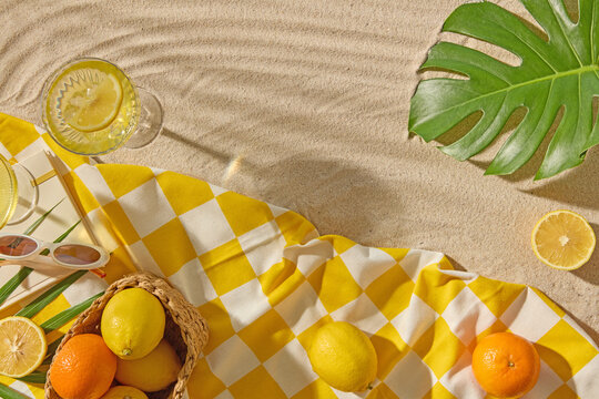 Bright summer picnic flatlay with citrus basket, tropical leaves, sunglasses, and refreshing drinks on a yellow checkered cloth, perfect for travel and product presentation.