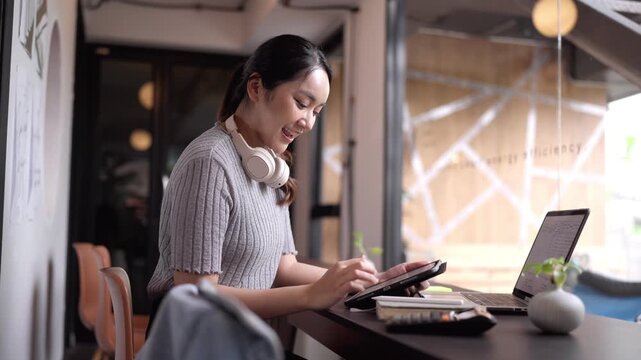 Asian freelance woman celebrates online business achievement working remotely from modern cafe coworking space digital nomad success