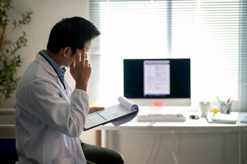 doctor is sitting at a desk with a computer monitor and a clipboard