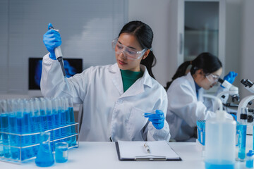 Scientist using micropipette dropping blue liquid in laboratory