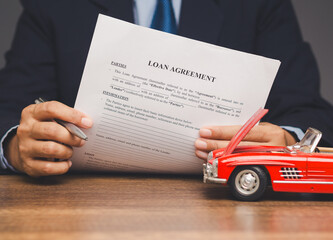 Businessman signing car loan agreement with red toy vehicle symbolizing auto finance and approval.