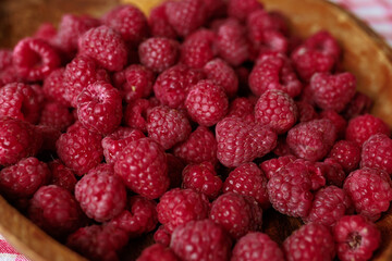 A wooden bowl with ripe raspberries lies on a rustic tablecloth.