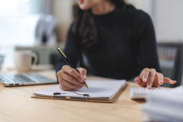 Businesswoman calculating and writing notes in office using calculator and pen