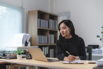 Young asian businesswoman taking notes while attending a video conference in office