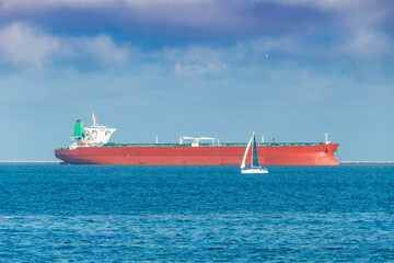 Sailboat moving pass a container ship anchor out in the harbor

