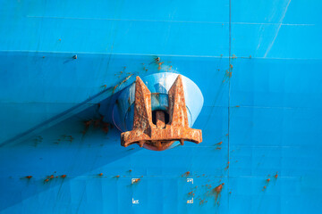 Rusted anchor hanging off a blue colored ship