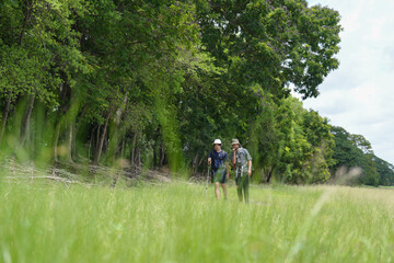 Fototapeta premium Happy tourist hiking walking together over grassland of the plains. Active young adult man trekking through nature grass field over lowland in rural trail. Portrait of real people in peaceful meadow.