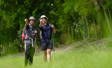 Happy tourist hiking walking together over grassland of the plains. Active young adult man trekking through nature grass field over lowland in rural trail. Portrait of real people in peaceful meadow.