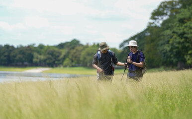 Obraz premium Happy tourist hiking walking together over grassland of the plains. Active young adult man trekking through nature grass field over lowland in rural trail. Portrait of real people in peaceful meadow.