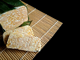 Close-up of tempeh, a traditional Indonesian fermented soybean cake, partially wrapped in banana...