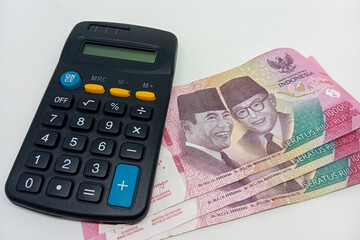 A dark colored calculator with yellow and blue buttons rests beside several Indonesian 100,000...