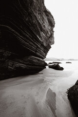 Stratified Rock Formation on Coastal Beach in Black and White. Footprints in sand add human element...