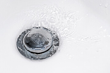 Water flowing down into a drain in bathroom sink. Concept of hygiene, cleaning, sanitation and...