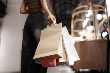 Stylish young woman walking outdoors at night, carrying shopping bags with joy, surrounded by city...