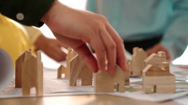 Architect and engineer discuss about building blueprint on table with architectural document, measurement tools scatter around at office, use wooden block for house positioning. Closeup. Delineation.