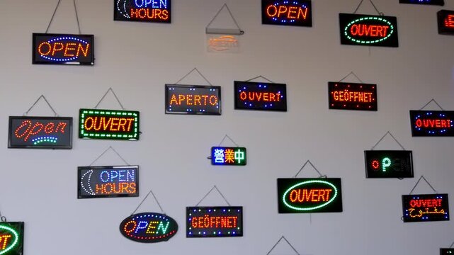 Colorful neon "open" signs in multiple languages hanging on a white wall, creating a vibrant and multicultural visual mosaic
