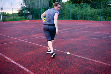 Obraz premium Woman practicing soccer drills on a red sports field. She's dribbling the ball towards a marker.
