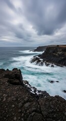 Obraz premium Dramatic coastal landscape with waves crashing against the rocky cliffs under a cloudy sky