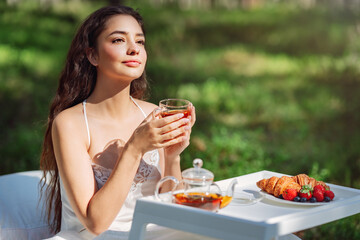 Woman wakes up in a summer forest. Young woman has breakfast in bed in a summer forest