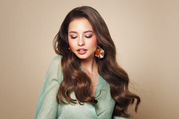 Brunette girl with perfect makeup. Smiling beautiful model woman with long curly hairstyle. Care...