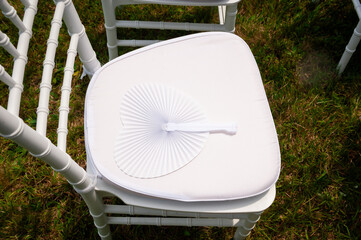 White chair with fan at an outdoor wedding ceremony