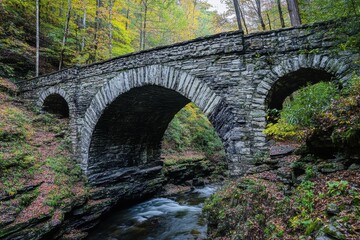 A stone bridge with arches over a river in a forest during the autumn season with colorful trees