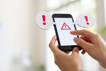 A person holding a phone with a warning sign and exclamation marks on the screen and around it