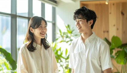 柔らかな日差しが差し込む現代的なオフィスで仕事の話をする若い男女、観葉植物と木材が映える背景


