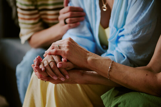 Cropped shot of unrecognizable women gently holding hands, showing support and empathy during emotional moment, partial body visible