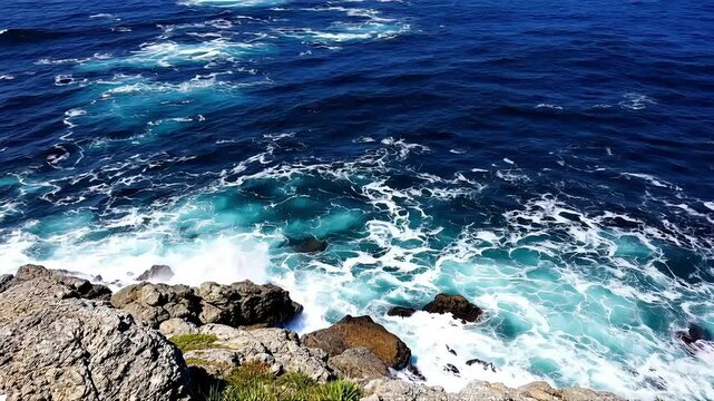 Blue ocean waves crash against rugged coastal rocks under a vast sky, A rocky coastline with deep blue water and crashing waves, High-quality landscapes nature video footage 