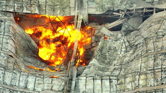 Aerial drone view reveals an intense blaze consuming the structure, flames tearing through the roof and exposing molten debris, capturing the scale and destructive force of the fire.
