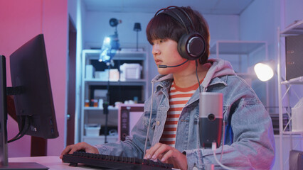 Young Asian gamer boy is excited playing online video games on gaming computer with keyboard and headset, cyber virtual technology, esports entertainment in dark room, fun teenage streaming lifestyle. © tigercat_lpg