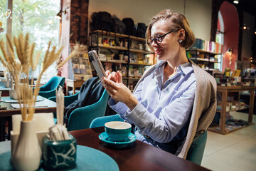 woman looking at smartphone and drinking coffee in restaurant