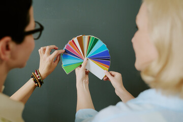 Caucasian middle aged women holding and discussing color swatch palette together, hands and partial...