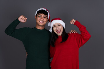 Fototapeta premium Portrait of Excited Young Asian Couple Wearing Santa Hat, Christmas Holiday Concept