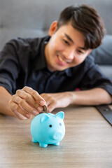 Young Asian man saving money putting coin into piggy bank, finance and budget planning concept