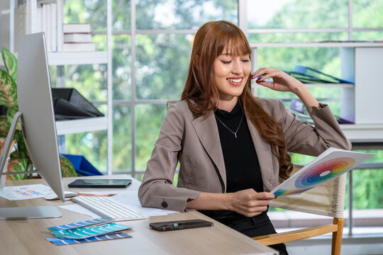 Asian female graphic designer smiling while holding color wheel in creative office workspace - Powered by Adobe