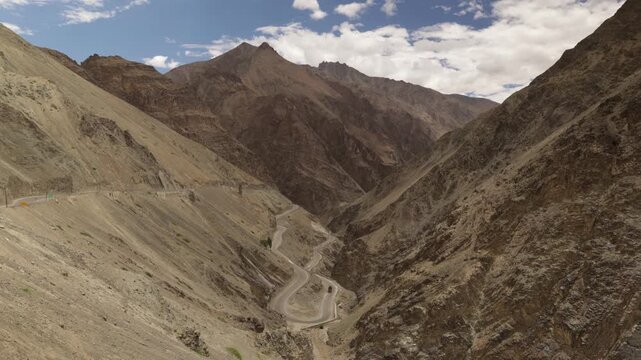 Main road from Kargil to Leh traffic on bendy road through rocky valley. Timelapse of cars and motorbikes winding through landscape looks like toys.