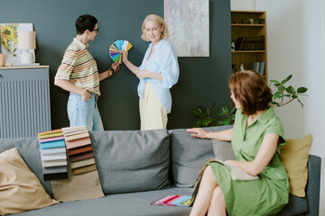 Middle aged Caucasian woman standing and holding color swatches while talking to another woman as...