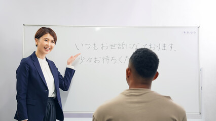 A female teacher teaches business terms to a black man at a Japanese language school.