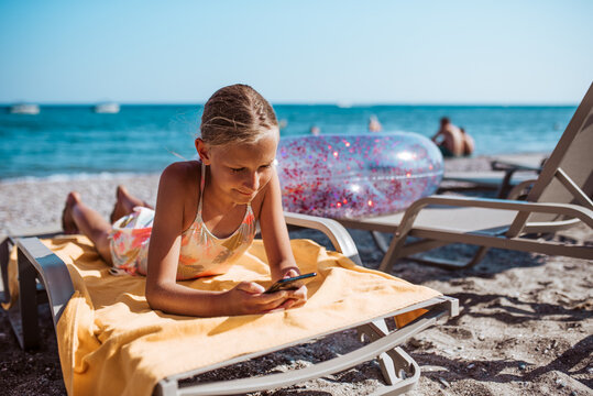 Gril relaxing on beach lounger with smartphone in hand.