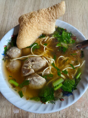 Close-up top view of asian noodle soup with meatballs, vegetables, and crispy cracker in flavorful broth served in bowl