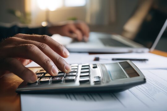 A person uses a calculator while sitting at a laptop, working