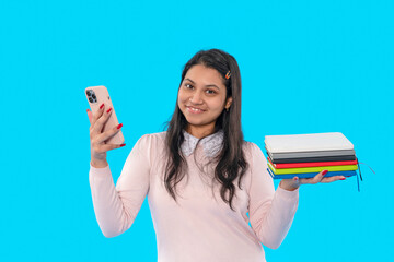 Young woman smiling while holding notebooks and phone against a bright blue background in a...