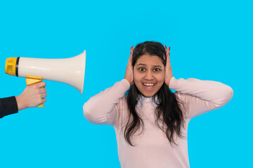 Person reacts with surprise while covering their ears from a loudspeaker on a vibrant blue...