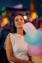 Young woman holding cotton candy at night in amusement park