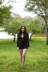 Young and beautiful woman with long hair and sensual black dress walks through the forest among trees and green grass and makes different body expressions in her passage in nature.