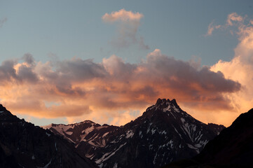 A night view of snowy mountains with clouds at sunset. The clouds and sky turn a magnificent golden color as the sun sets.
