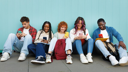 Students using smartphones sitting on the ground against a light blue wall