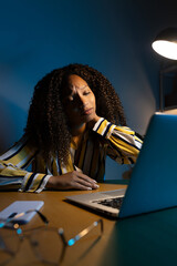 Vertical portrait of Black woman suffering from neck pain, working late at night using laptop